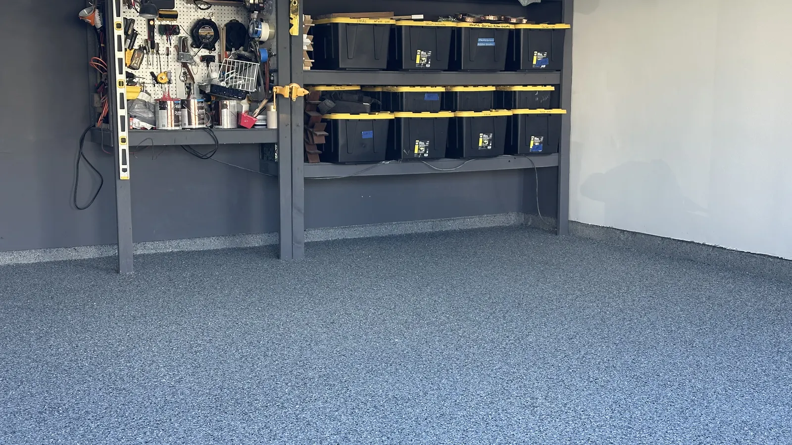 Finished gray and blue polyaspartic flake garage floor with workbench and storage bins along the back wall