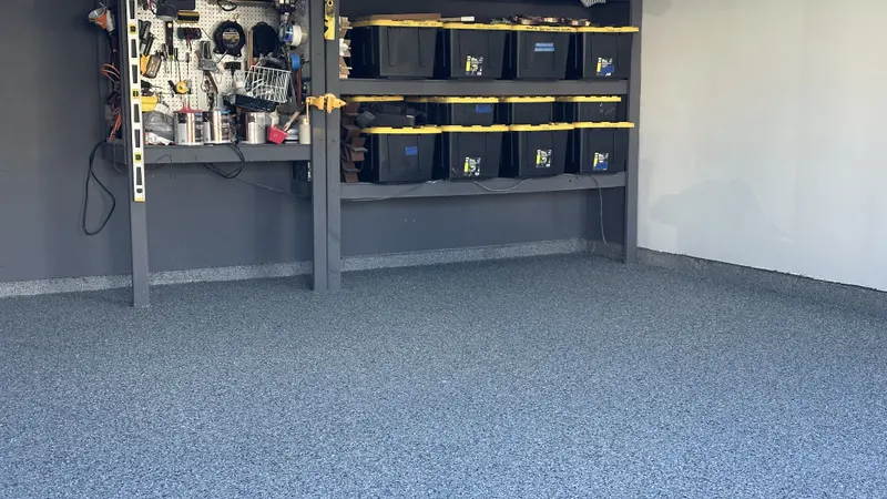 Finished gray and blue polyaspartic flake garage floor with workbench and storage bins along the back wall