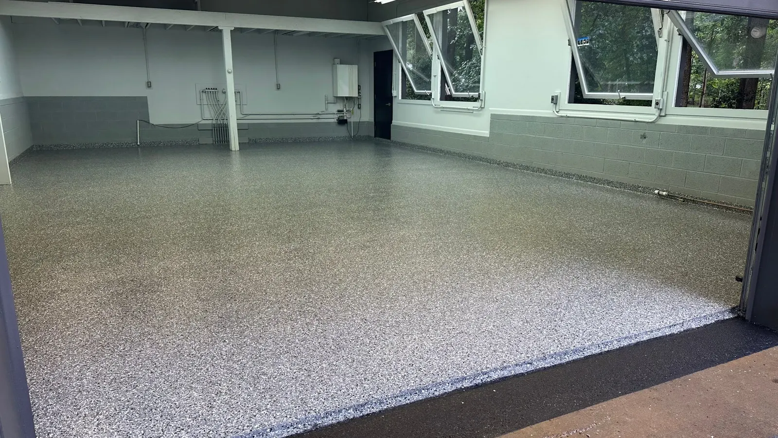 Gray and white polyaspartic flake floor filling a clean, empty garage with block walls and windows