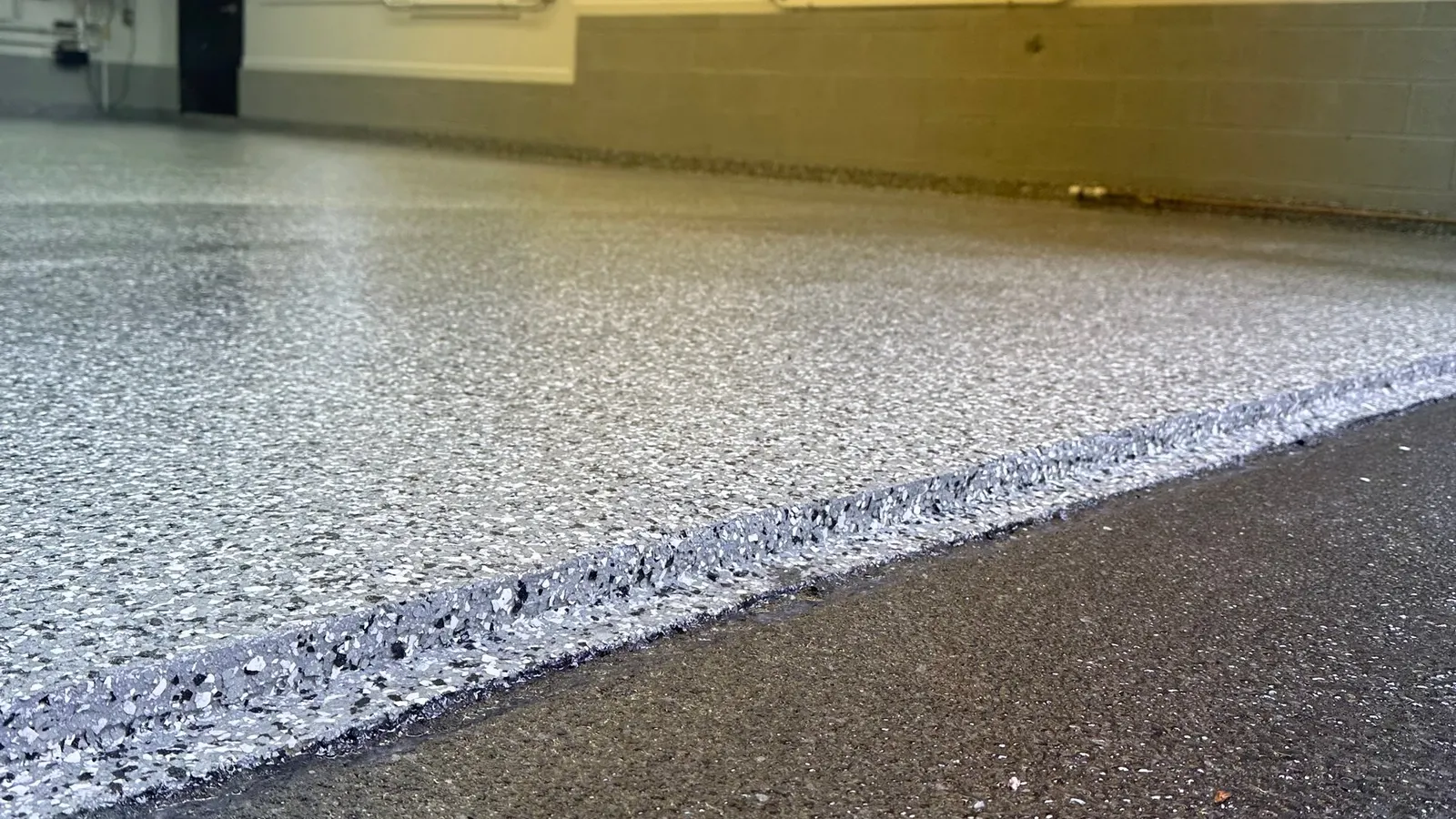 Low-angle view of a finished gray polyaspartic flake garage floor meeting the driveway at the door edge
