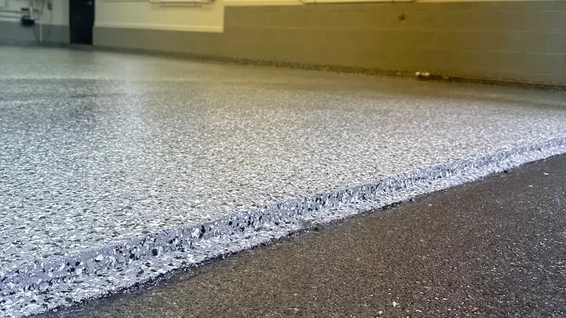 Low-angle view of a finished gray polyaspartic flake garage floor meeting the driveway at the door edge