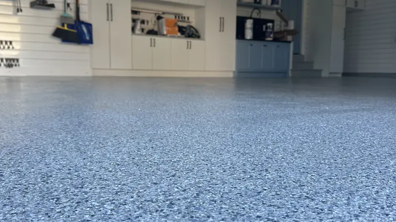 Low-angle view of a finished blue-grey polyaspartic flake garage floor with white storage cabinets behind.