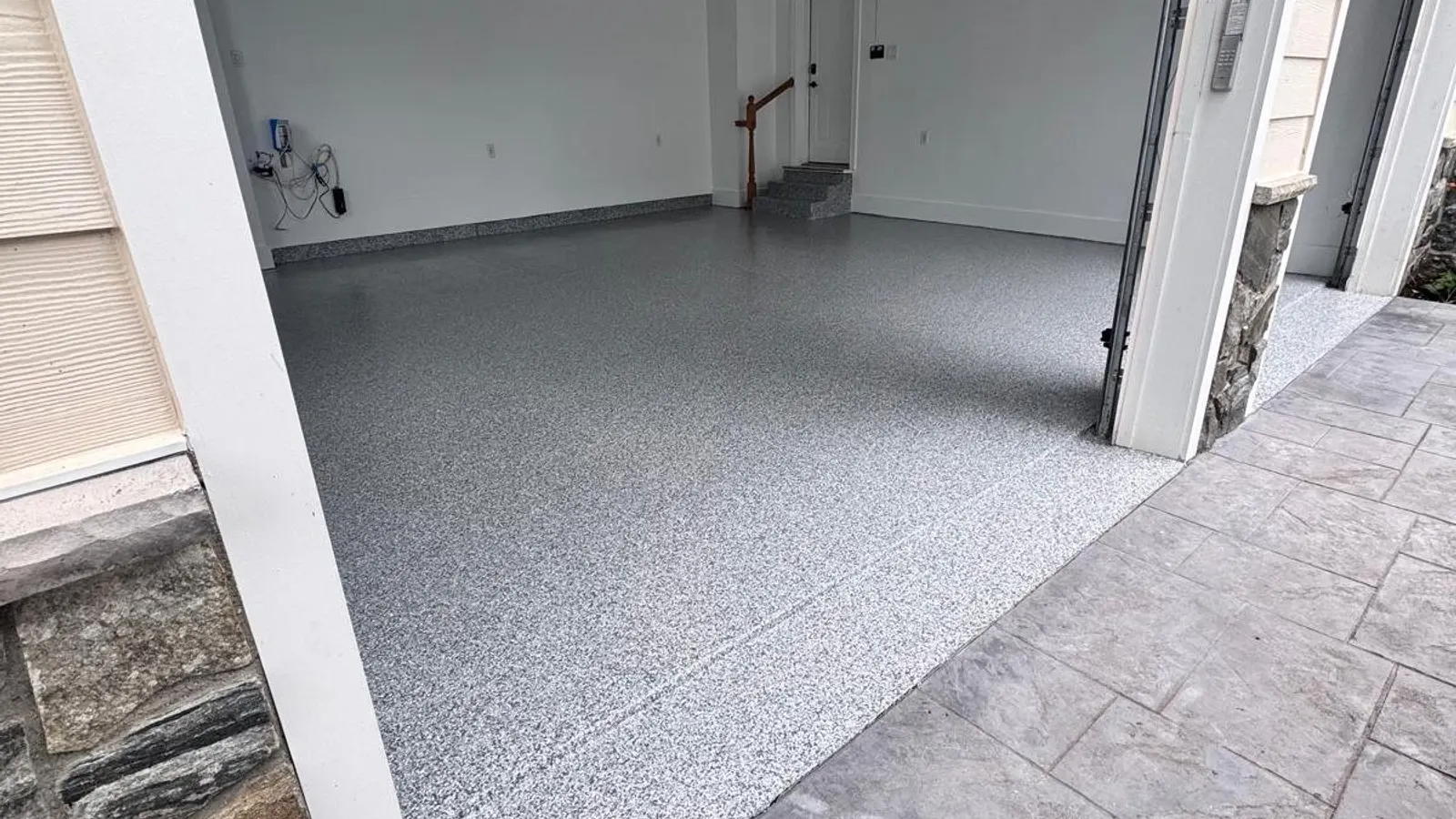 Empty garage with a finished gray and white polyaspartic flake floor viewed from the driveway.